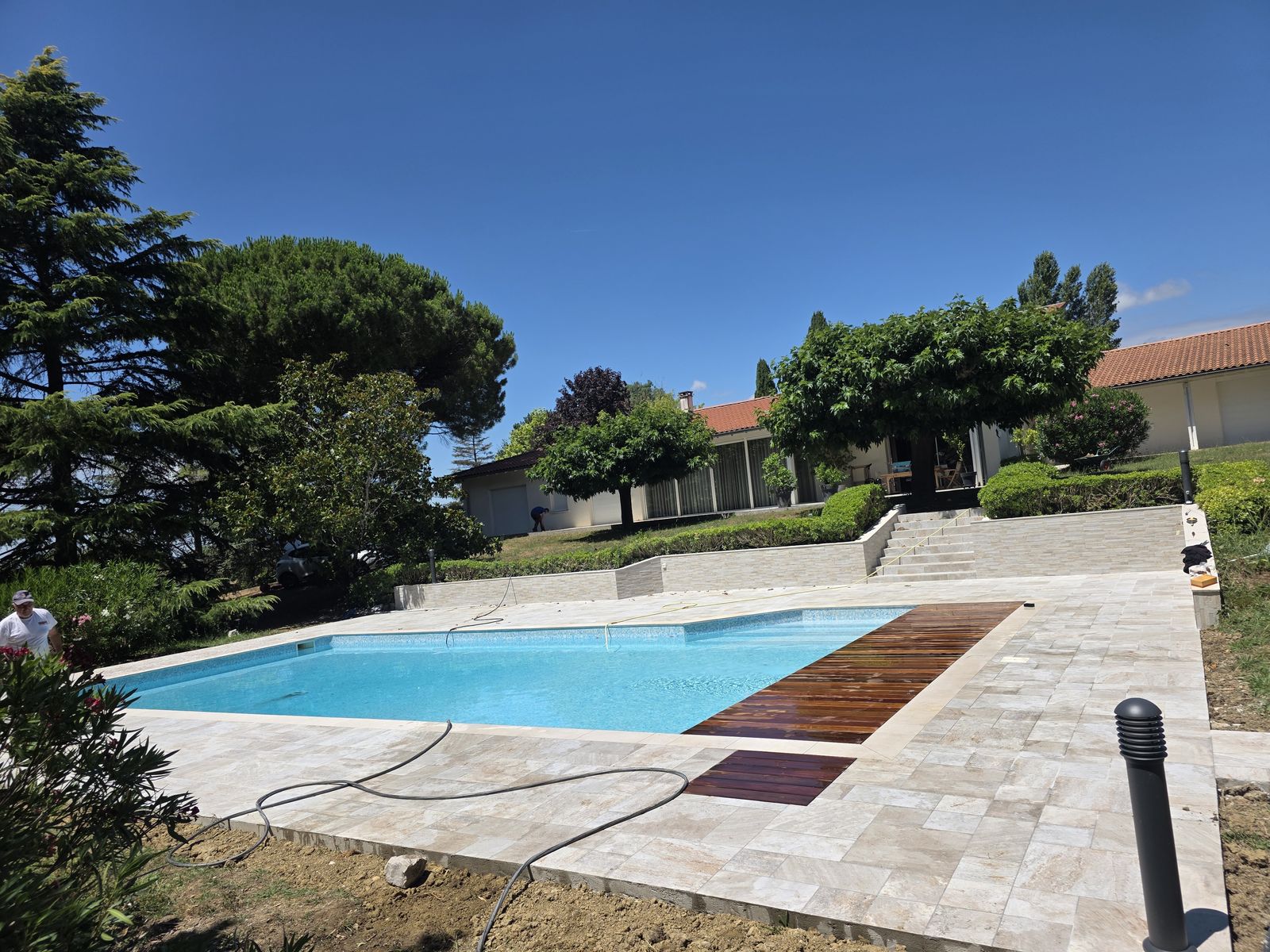 Plage de piscine en travertin avec deck bois réalisée par RGBAT